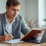 Pessoa organizando investimentos no notebook e anotando metas financeiras em um caderno de planejamento.