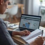 Pessoa montando um orçamento pessoal no notebook e anotando metas de gastos e economia em um caderno organizado.